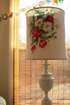 a white lamp with flowers painted on it sitting in front of a window sill