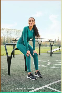 a woman sitting on top of a bench in front of a playground with an empty basketball court