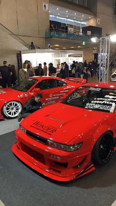 two red sports cars parked next to each other in a showroom filled with people