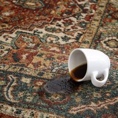 a white coffee cup sitting on top of a carpet covered in oil and water next to a rug