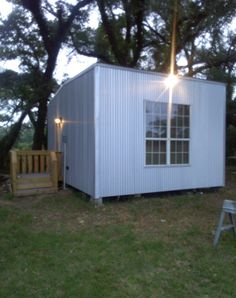 a small white shed sitting on top of a grass covered field next to a tree