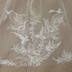 an embroidered veil with white flowers and leaves on the bottom is laying on a wooden floor