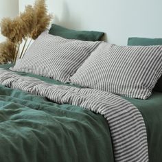 a bed with green sheets and pillows on top of it next to a plant in a vase