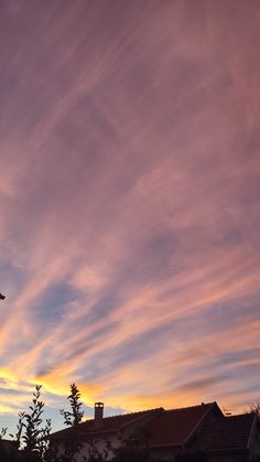 an airplane is flying in the sky at sunset with clouds and trees around it as the sun sets