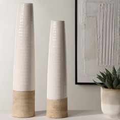 three white vases sitting on top of a table next to a potted plant