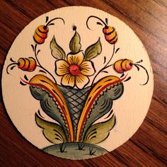 a painted wooden plaque with flowers and bees on it's side, sitting on a table