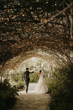 a bride and groom holding hands under an archway with lights on the ceiling at their wedding