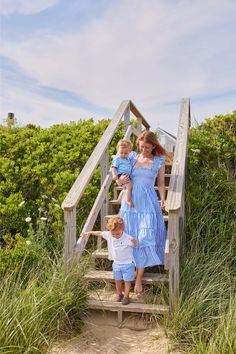 a woman and two children are standing on stairs in the sand at the beach with grass