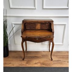 an old wooden desk sitting on top of a hard wood floor next to a potted plant