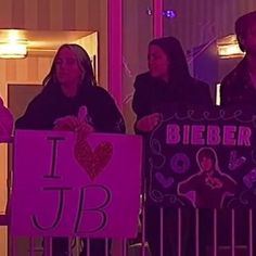 some people holding signs in front of a building with lights on and one woman is wearing a black jacket