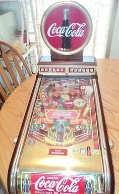 an old fashioned coca cola machine sitting on top of a table next to a chair