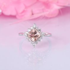 a pink diamond ring sitting on top of a white table next to some pink flowers