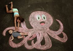 a woman and child laying on the ground next to an octopus drawn in chalk with colored crayons