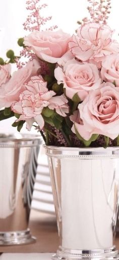 pink flowers in silver cups sitting on a table with plates and utensils behind them