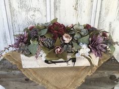 a wooden box with flowers and greenery in it on a burlap cloth