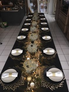 a long table is decorated with black and white plates, silverware and gold trimmings