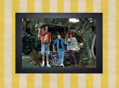 three people are standing in front of a rock wall and some trees, one is wearing mickey mouse t - shirts