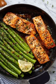 salmon and asparagus in a skillet with lemon wedges