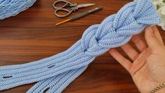 a hand holding a blue rope with scissors and yarn next to it on a table