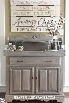 an old dresser is painted gray with white lettering and flowers in vases on top