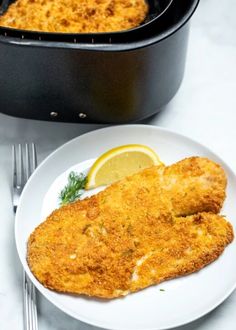 a white plate topped with fried fish next to a skillet filled with sauce and lemon wedges