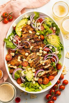 a salad with chicken, tomatoes, onions and lettuce in a white bowl