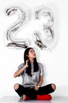 a woman sitting on the floor in front of balloons and number twenty five balloon letters