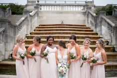 a group of women standing next to each other in front of a fountain holding bouquets