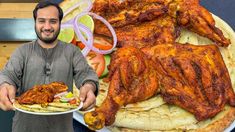 a man holding a plate with chicken wings on it next to a large platter of food