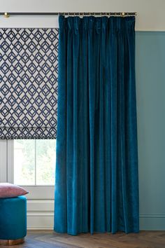 the curtains in this living room are blue and have diamond patterns on them, along with a pink footstool