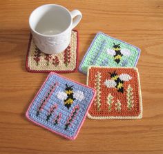 three square crocheted coasters on a wooden table with a coffee cup and mug