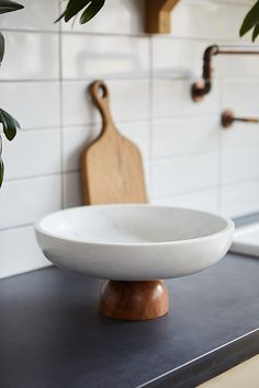 a white bowl sitting on top of a counter next to a cutting board and potted plant