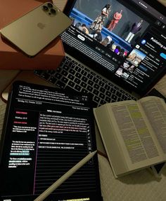 an open laptop computer sitting on top of a table next to a book and cell phone