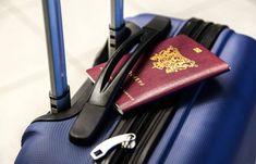 a red passport sitting on top of a blue suitcase