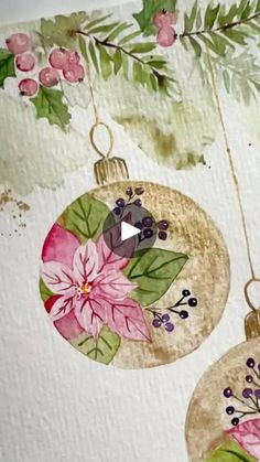 two ornaments hanging from a tree branch with leaves and flowers painted on the inside of them