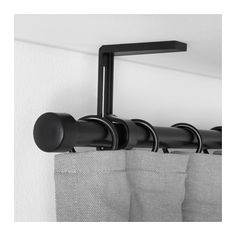 the curtain rod is attached to the wall by two black hooks, and hangs from the ceiling