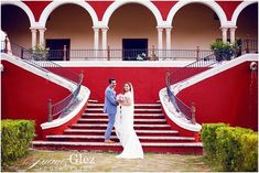 a bride and groom standing in front of a red building with steps leading up to it