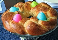 a bundt cake decorated with colored eggs on a glass platter next to a white plate