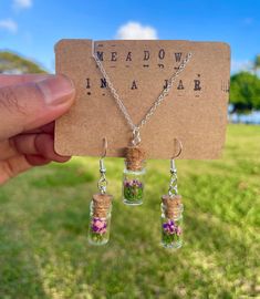 a person holding up a tiny bottle with flowers in it and two necklaces attached