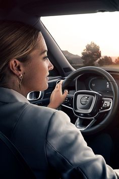 a woman driving a car with her hand on the steering wheel and looking at the dashboard