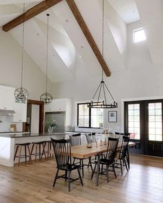 a large open kitchen and dining room area with wood flooring, white walls and ceiling beams