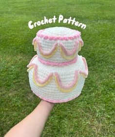 a hand holding a crochet cake on top of a green grass covered field