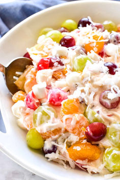 a white bowl filled with fruit salad on top of a marble counter next to a metal spoon