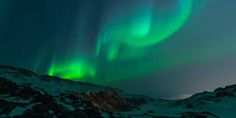 an aurora bore is seen in the sky above snow covered mountains