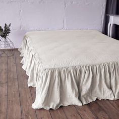 a bed with a ruffled bedskirt on top of it in front of a white brick wall