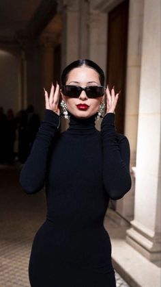 a woman in a black dress and sunglasses posing for the camera with her hands on her head