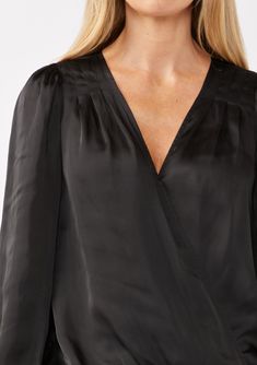 A soft and silky long sleeve holiday surplice blouse. Satin Relaxed fit Long sleeves Elastic wrist cuff Surplice v-neckline with hook & eye closure Elastic hemline Pleated shoulder details Women's holiday blouse Dry clean recommended or hand wash cold Step into the holiday season with elegance in our stunning surplice satin blouse, designed with a chic hook-and-eye closure, graceful long sleeves, and a comfortable elastic hemline. Whether you're headed to a family gathering or a corporate event, Holiday Blouse, Surplice Blouse, Blouse Satin, Blouse Designed, Holiday Blouses, Classic Blouses, Chic Top, Satin Blouse, Wrist Cuffs