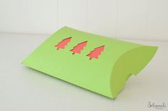 a green paper bag with cut out christmas trees on the front and sides, sitting on a white surface