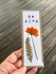 a hand holding up a card with an orange flower and the words be kind written on it