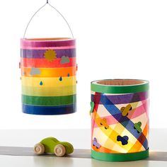 a rainbow colored tin can next to a toy car on a white surface with a string hanging from the ceiling